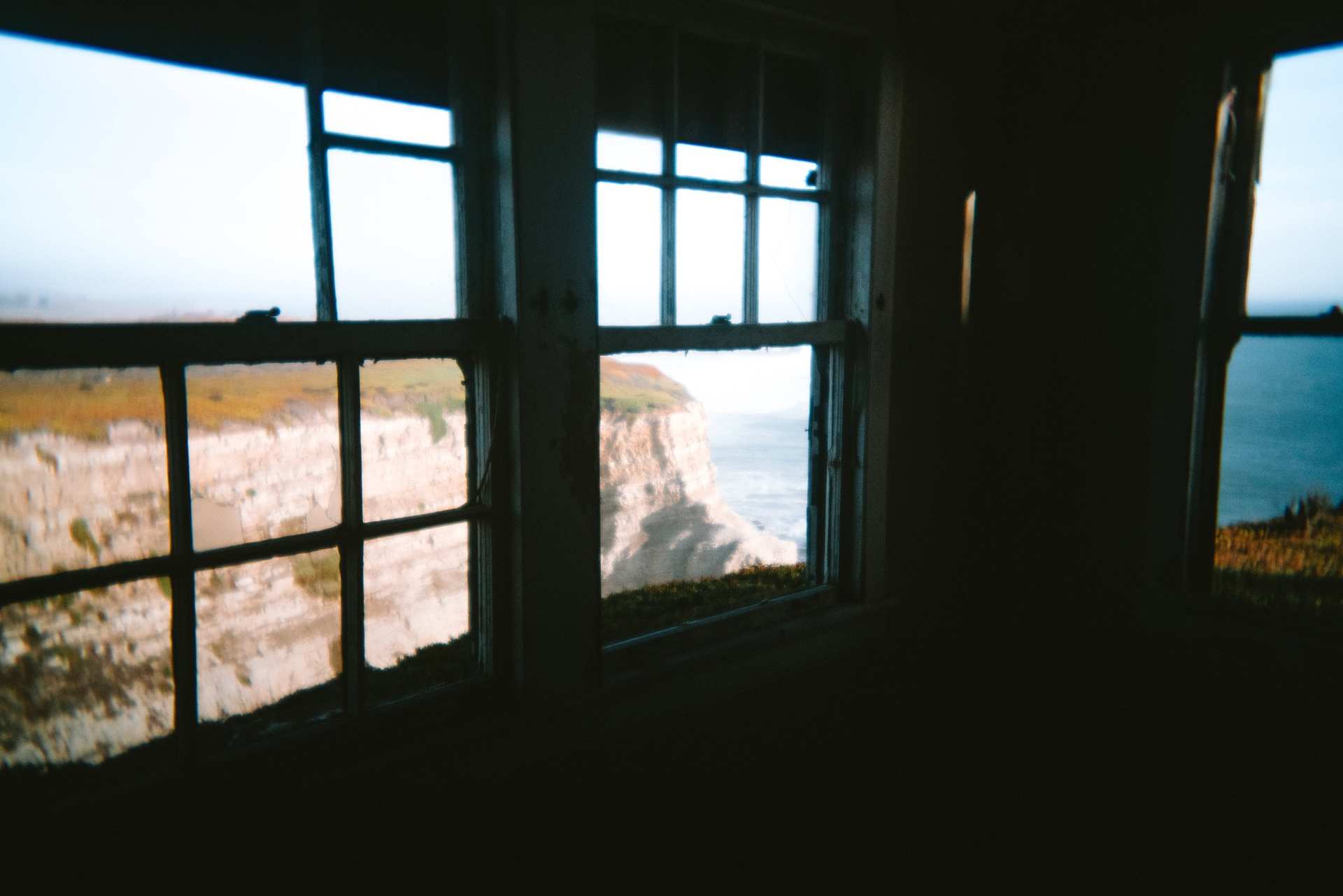 Sunlit coastal cliffs seen through the windows of a dark room.