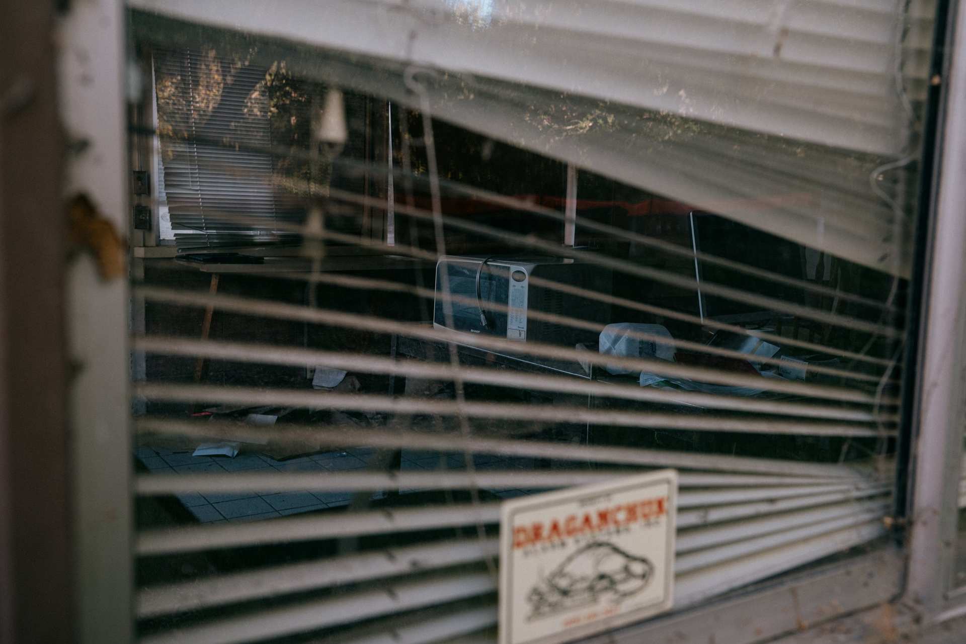 A weathered window with bent blinds and a small car sign on the sill.