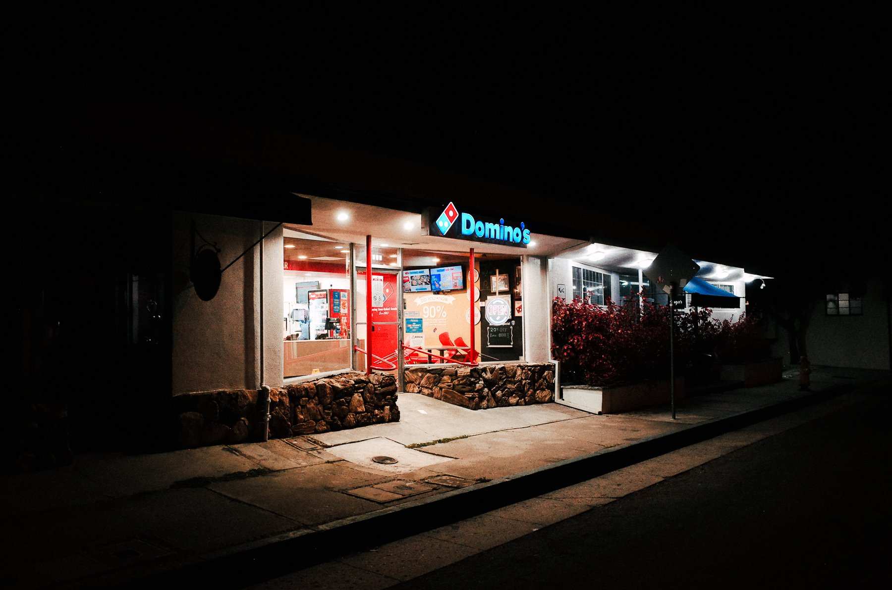 A brightly lit Domino’s storefront on a dark, empty street.