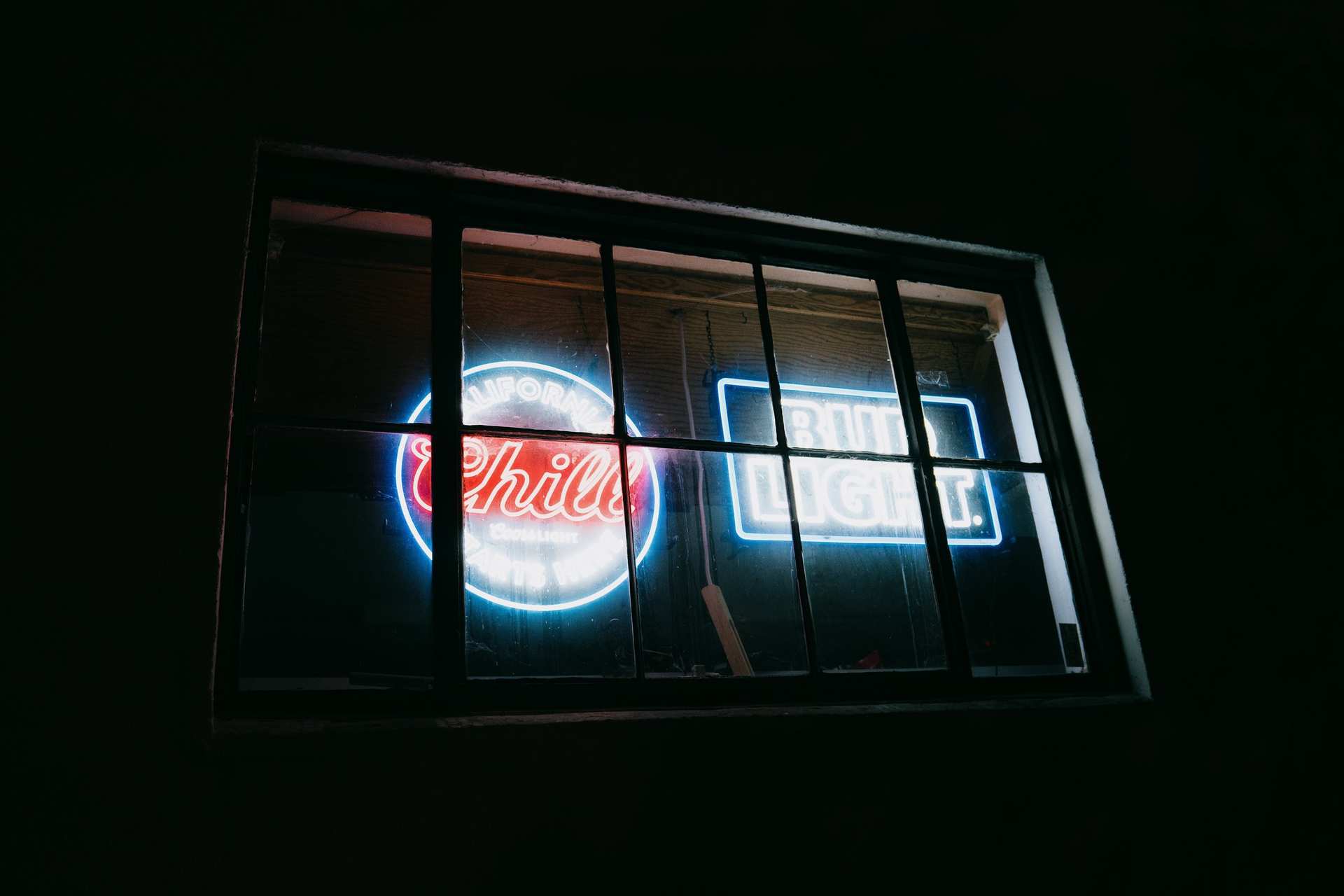 Blue and red beer signs glowing behind the bars of a dark window.