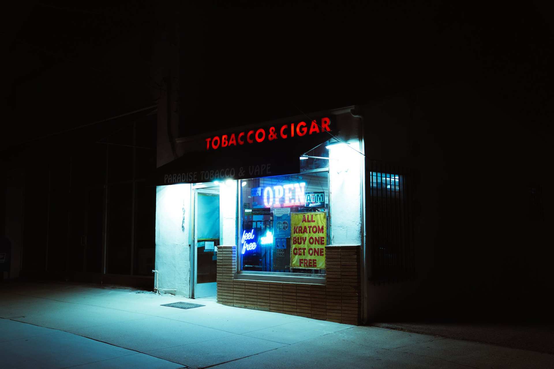 A tobacco shop at night, its bright doorway spilling light onto the sidewalk.